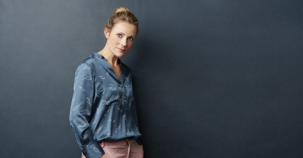 A plump woman in a blue shirt and pink pants leaning against a smooth wall.