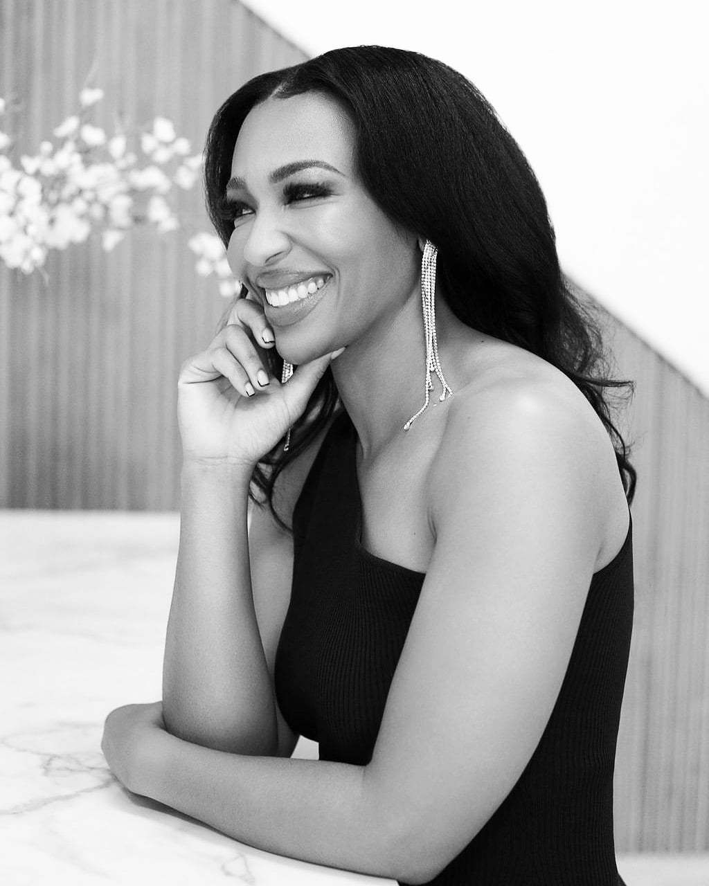 Black and white photo of a woman smiling in a black dress at home.