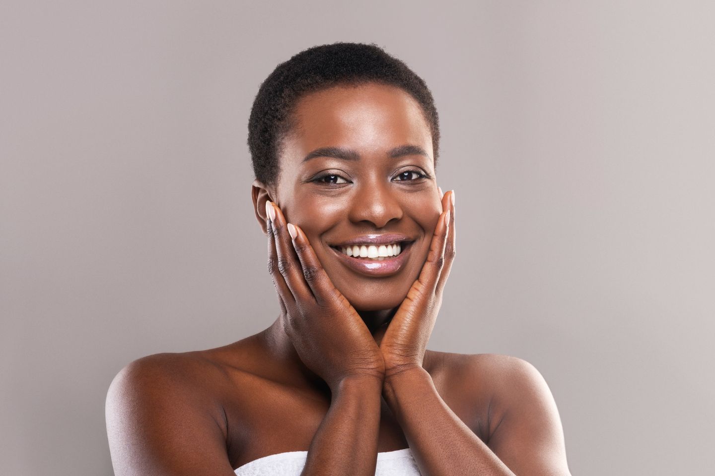 A young black woman smiling with her hands on her face.