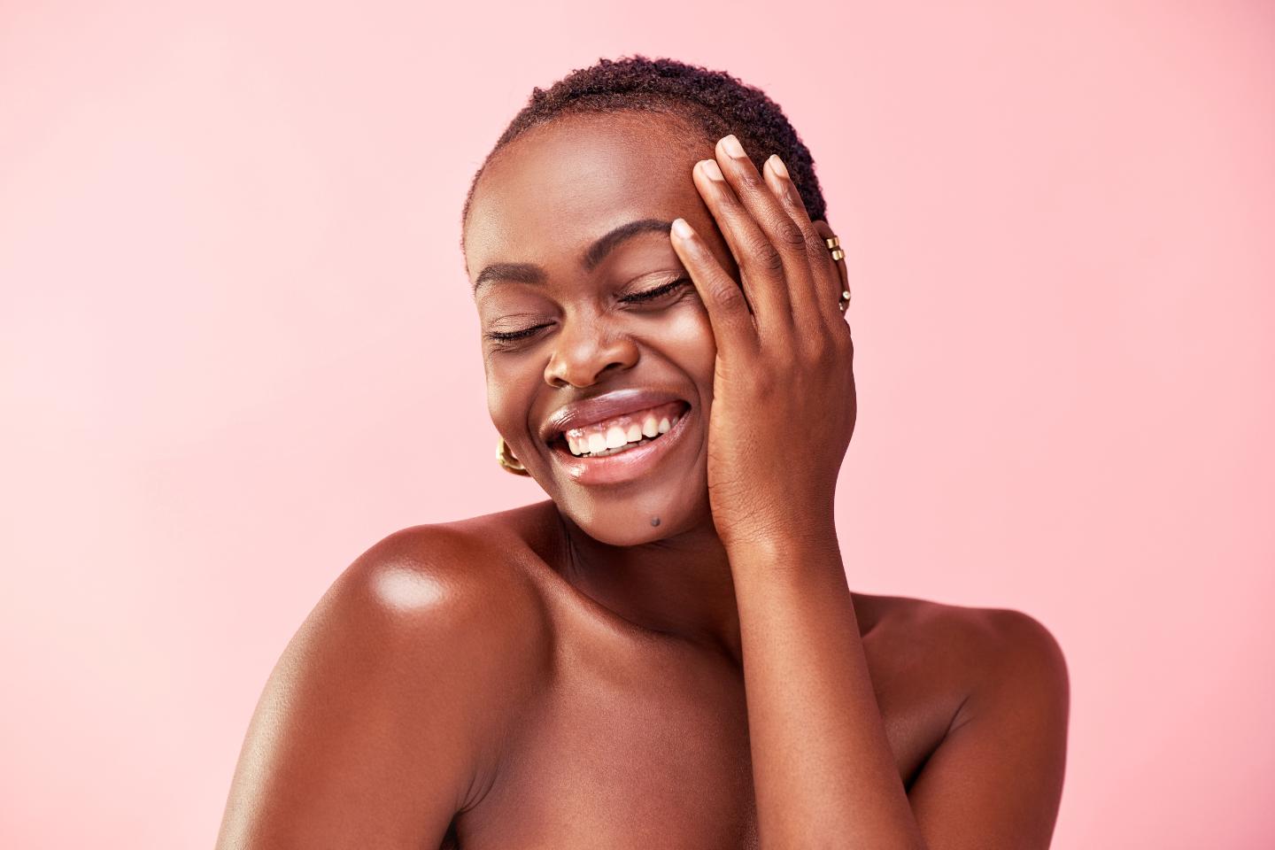 A black woman is smiling with her hands on her face, showcasing her refreshed and rejuvenated skin after undergoing a cosmetic procedure like microneedling.