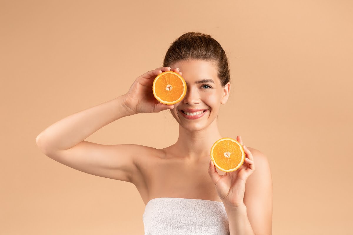 Woman holding orange slices up to her face, showcasing foods for healthy skin.