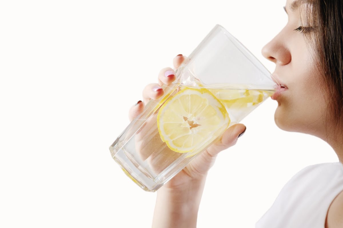 A person drinking lemon water, which is one of the foods for healthy skin, from a glass.