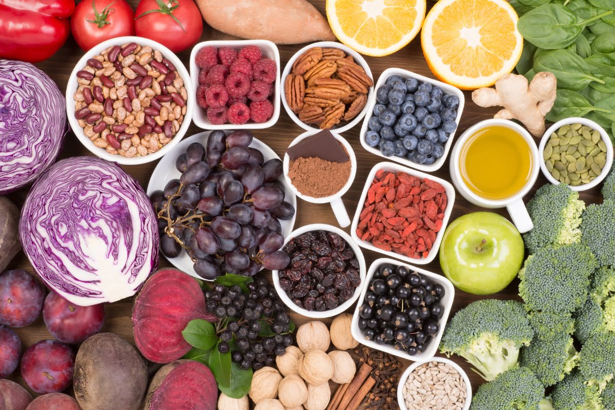 Assorted foods for healthy skin, including fruits, vegetables, nuts, and seeds displayed on a wooden surface.