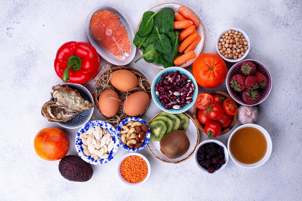 Assorted foods for healthy skin including fruits, vegetables, proteins, and whole grains arranged in bowls on a light background.