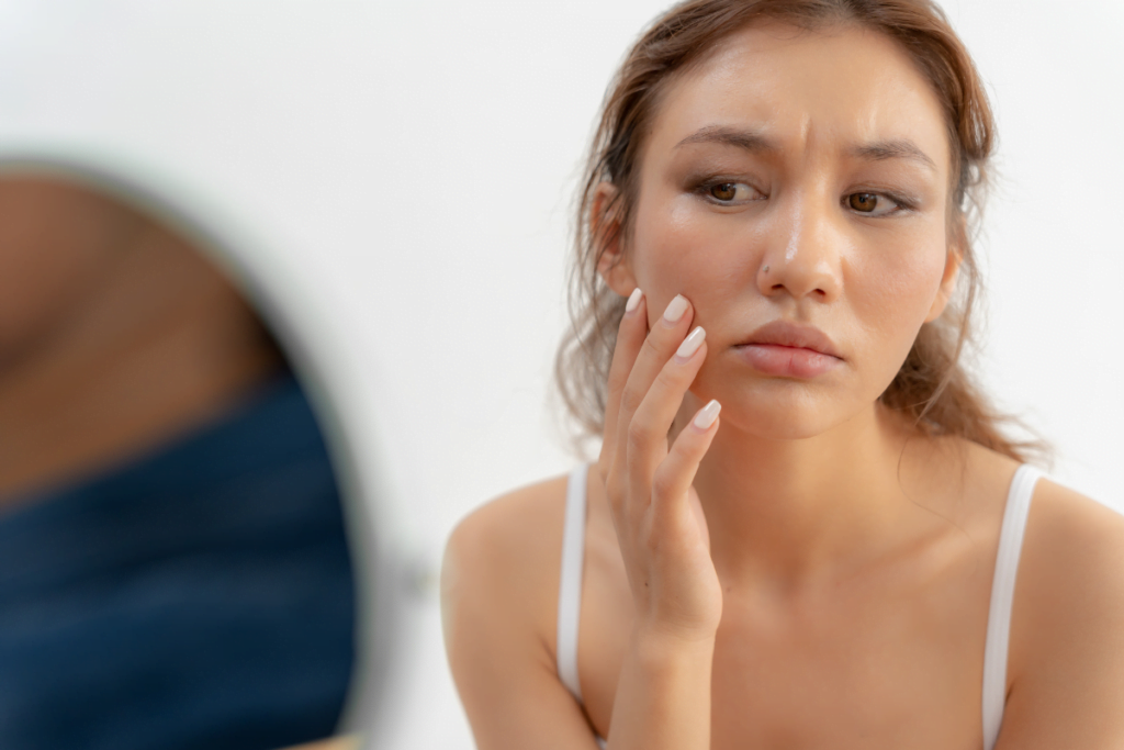 A woman is looking at her face in front of a mirror.