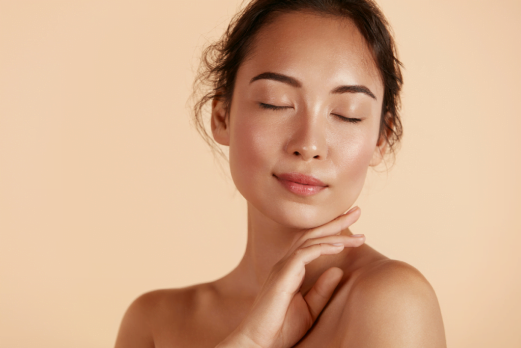 A woman with closed eyes enjoying the hydrafacial benefits, posing on a beige background.