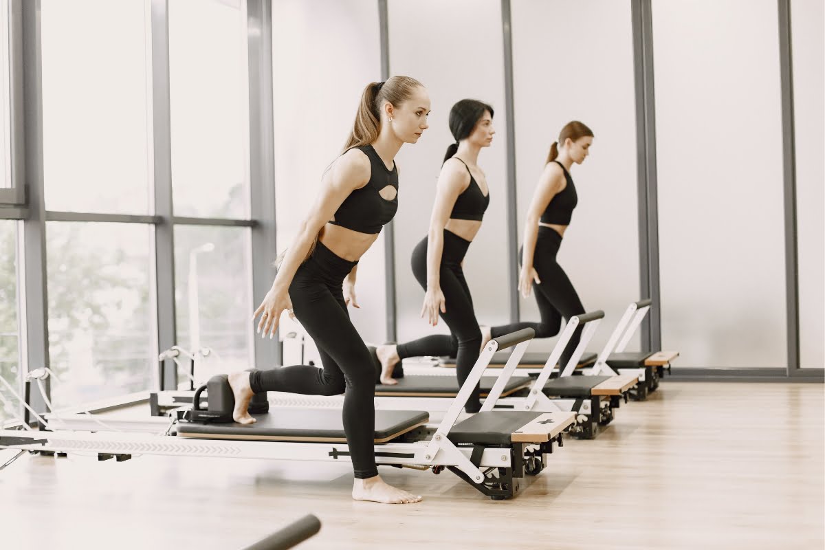 Two women realizing exercise benefits on pilates reformer machines in a bright, modern studio with mirrors.