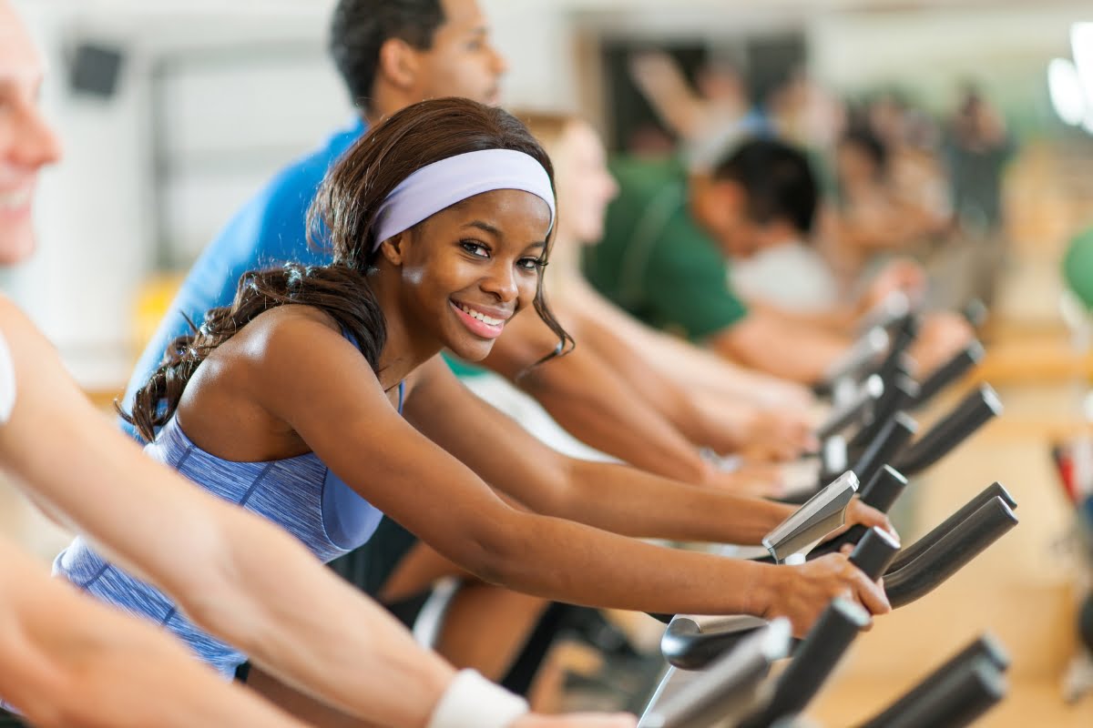 A diverse group of people smiling while enjoying the exercise benefits of using exercise bikes in a gym.