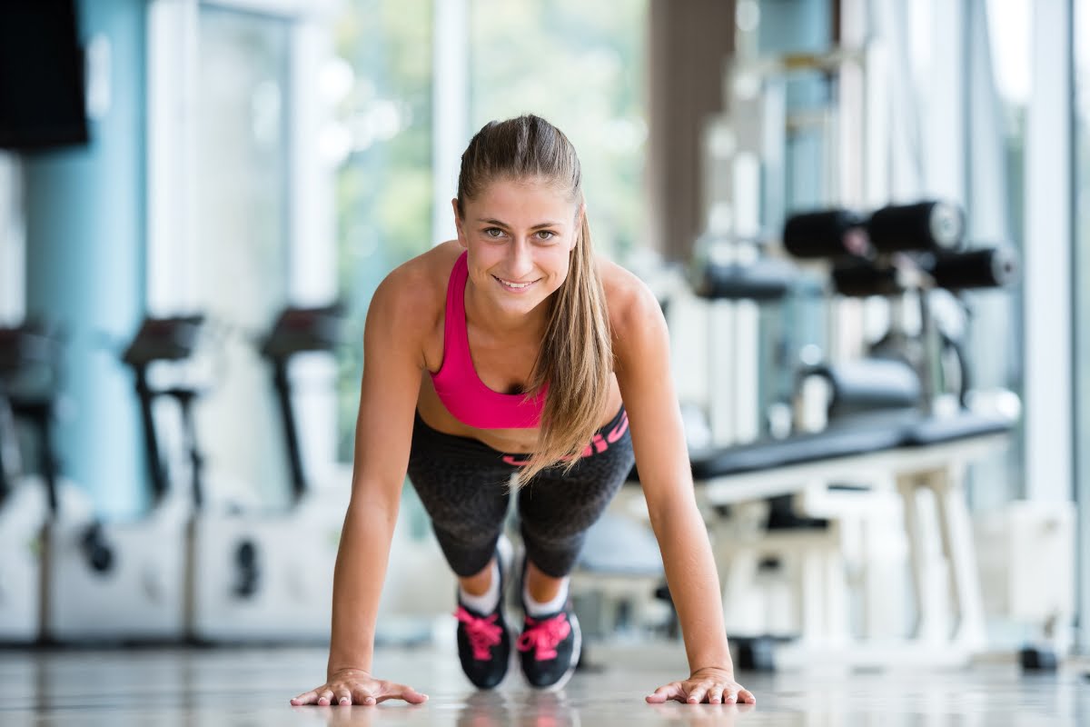 Woman smiling while doing push-ups in a sunny gymnasium, enjoying the exercise benefits.