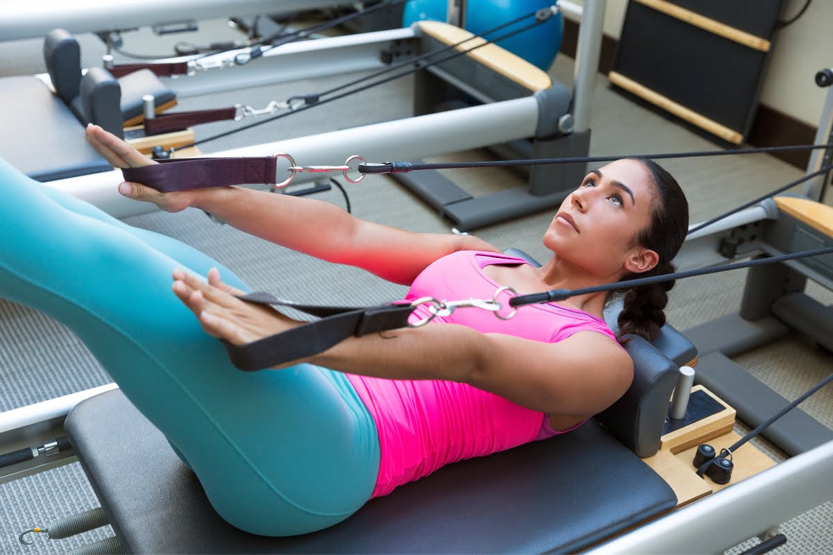 A woman experiencing the exercise benefits of working out on a Pilates reformer machine in a gym.