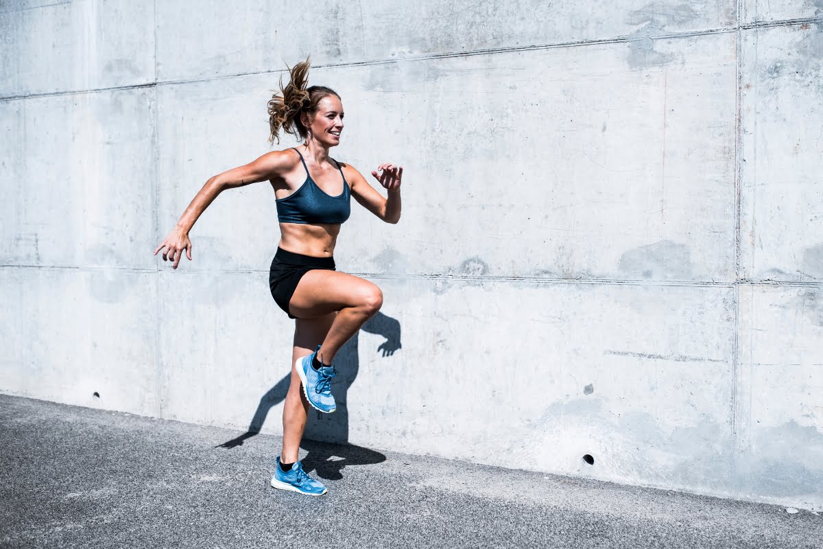 A woman in athletic wear running energetically against a concrete wall background, showcasing the exercise benefits.