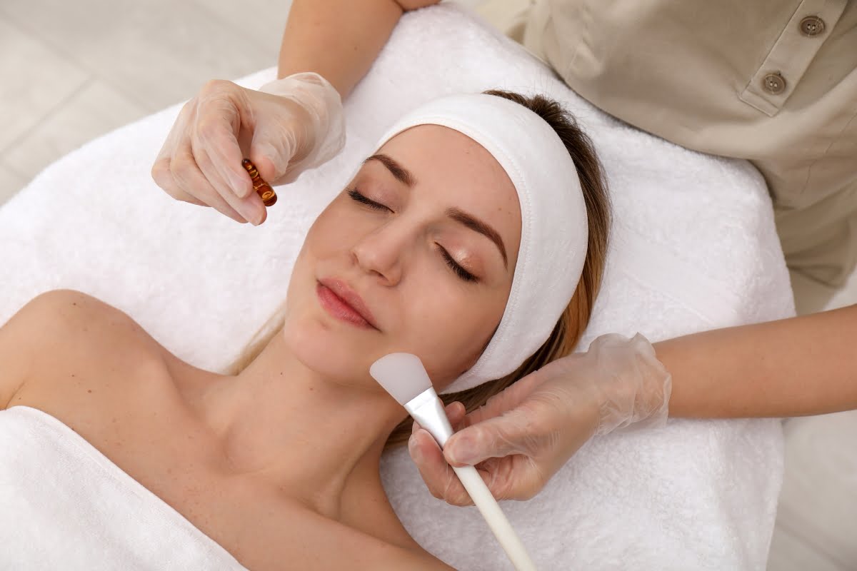 Aesthetician performing physical exfoliation treatment on a woman's face at a spa.