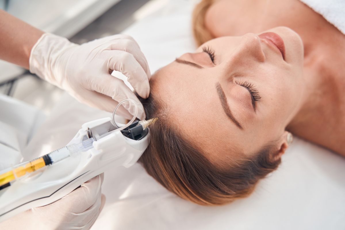 A person with eyes closed receives a scalp injection from a medical professional wearing white gloves. It's a scene that might prompt you to wonder, what is mesotherapy? This treatment involves administering vitamins and nutrients directly into the skin.