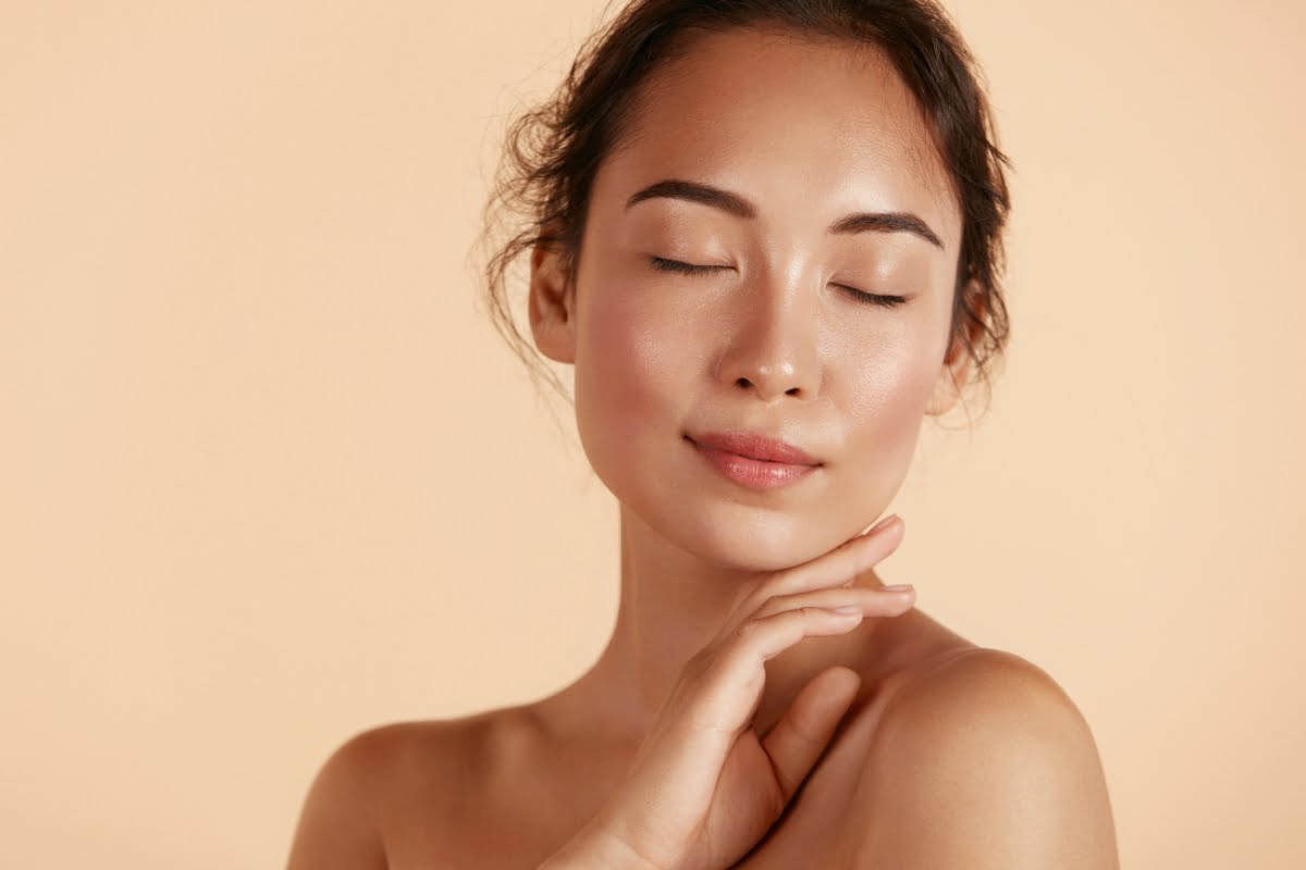 A person with closed eyes and a serene expression touches their face with one hand, emphasizing their skin's elasticity against a beige background.