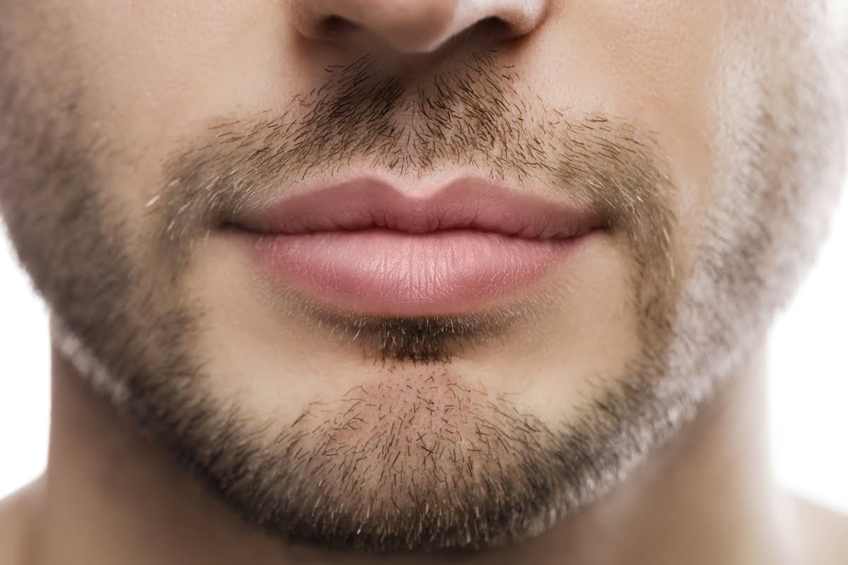 Close-up of a man's lower face, showing lips and short facial hair, against a white background. The subtle effects of skin fillers can be observed, enhancing the smoothness and youthfulness of his complexion.