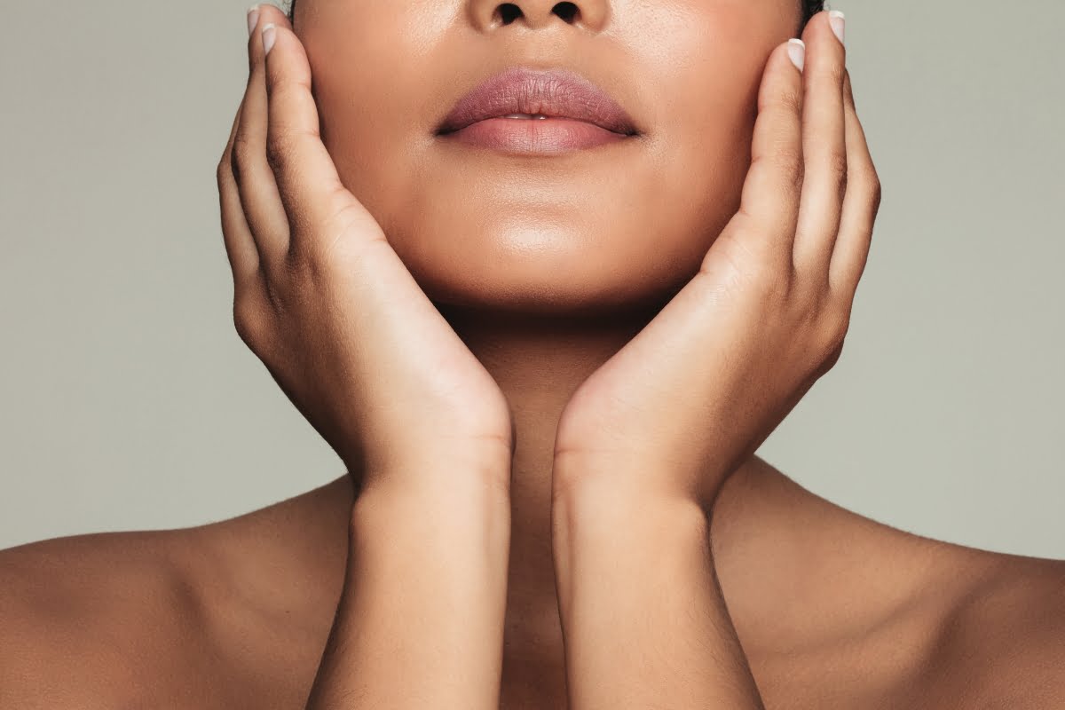 Close-up of a person's lower face and neck with hands gently cupping the jawline, displaying smooth skin and well-groomed nails, highlighting the visible microneedling benefits.