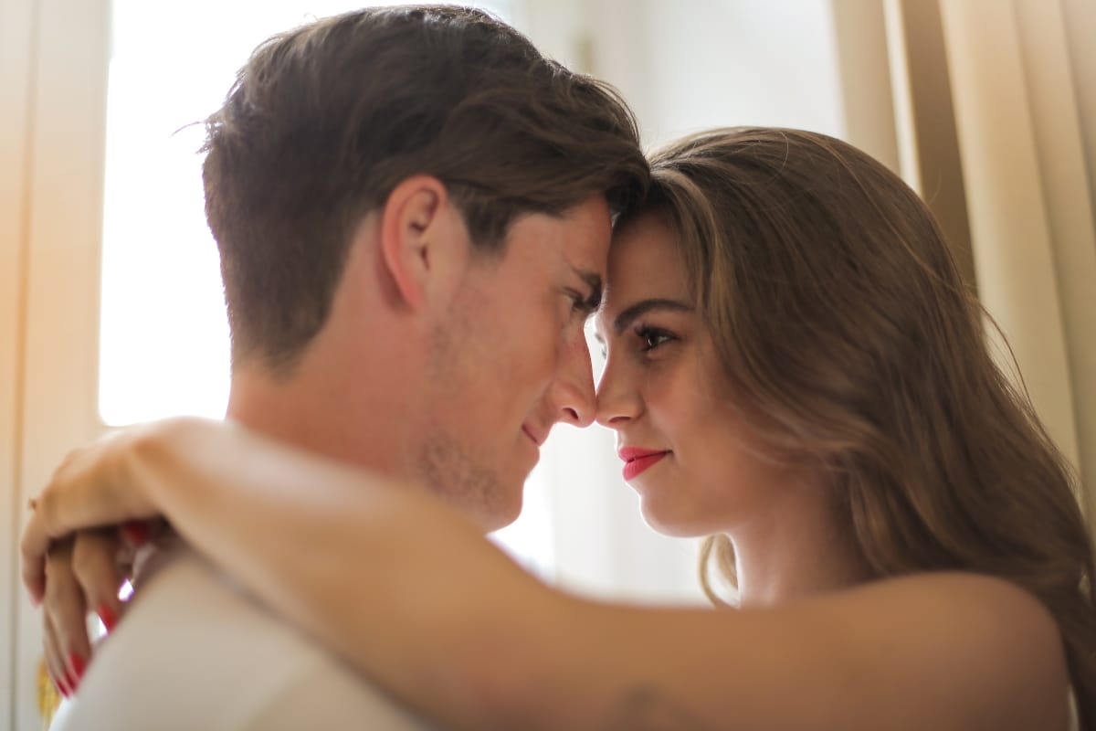 A man and a woman stand close, touching foreheads, and gazing into each other's eyes. The woman, who recently felt more confident after her non-invasive vaginal rejuvenation treatment, has her arms around the man's shoulders.