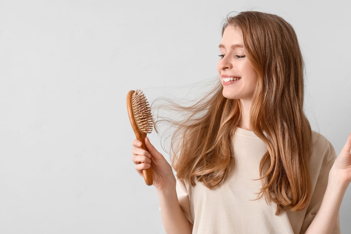 A woman smiling while brushing her long hair with a wooden hairbrush, radiating confidence after prp injections.